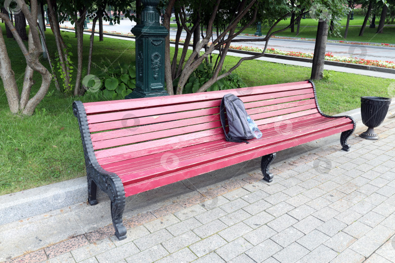 Скачать серый рюкзак и пластиковая бутылка лежат на красной скамейке в парке фотосток Ozero