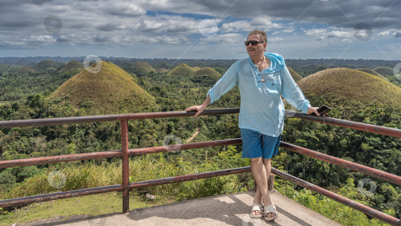 Скачать Мужчина стоит на смотровой площадке, улыбается, смотрит в сторону, облокотившись на перила. фотосток Ozero