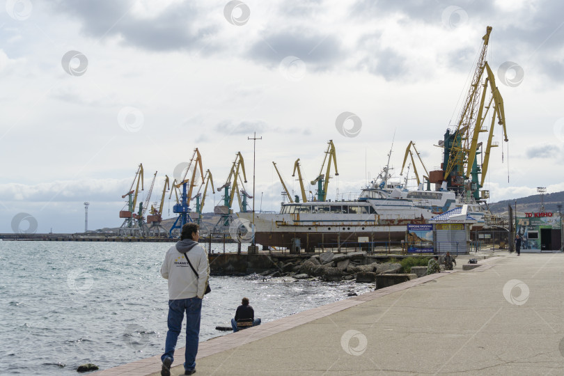 Скачать Грузовой порт Феодосии с кранами и кораблями. Вид с городской набережной. Феодосия, Крым, Россия - 26 сентября 2019 г. фотосток Ozero