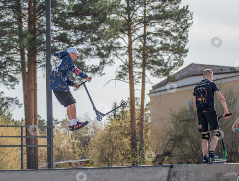 Скачать Россия, Красноярск 02 мая 2025г. Подросток на трюковом самокате в скейт-парке выполняет трюк во время прыжка. фотосток Ozero