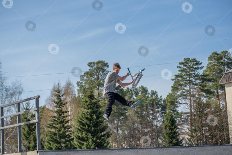 Скачать Россия, Красноярск 02 мая 2025г. Подросток на трюковом самокате в скейт-парке выполняет трюк во время прыжка. фотосток Ozero