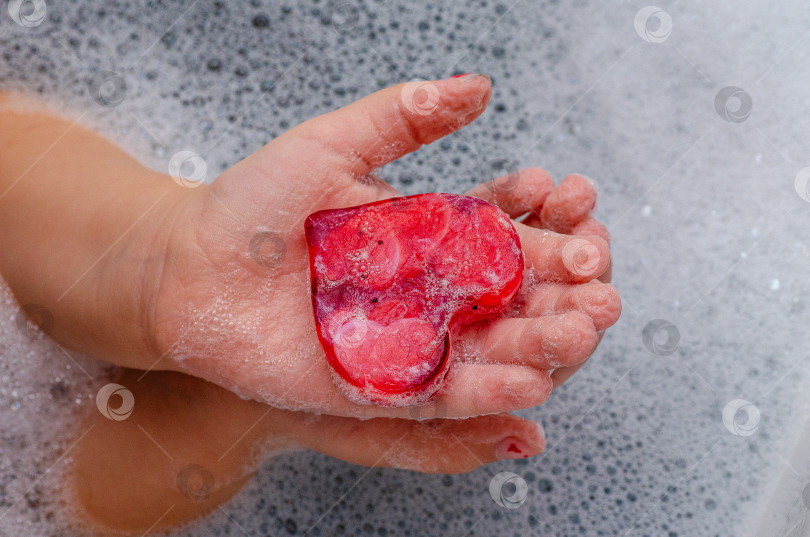 Скачать Детская ручка, держащая мыло в форме сердца с обильной пеной на светлом фоне фотосток Ozero