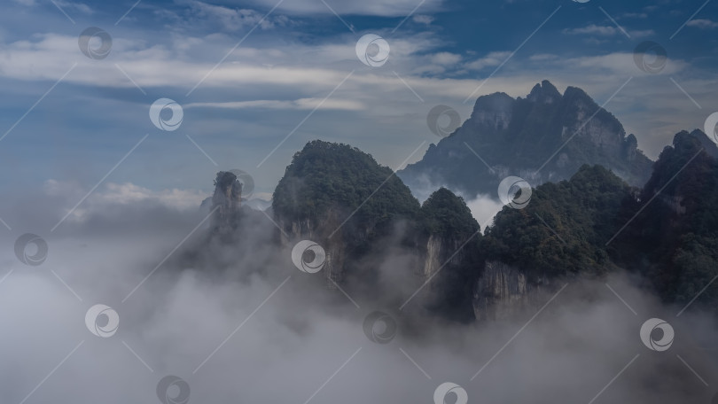 Скачать Вершины гор с зеленой растительностью и отвесными скалами возвышаются над облаками фотосток Ozero