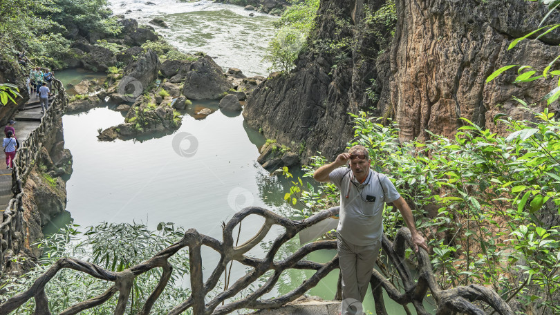 Скачать Мужчина в солнечных очках стоит на смотровой площадке у реки, облокотившись на перила фотосток Ozero
