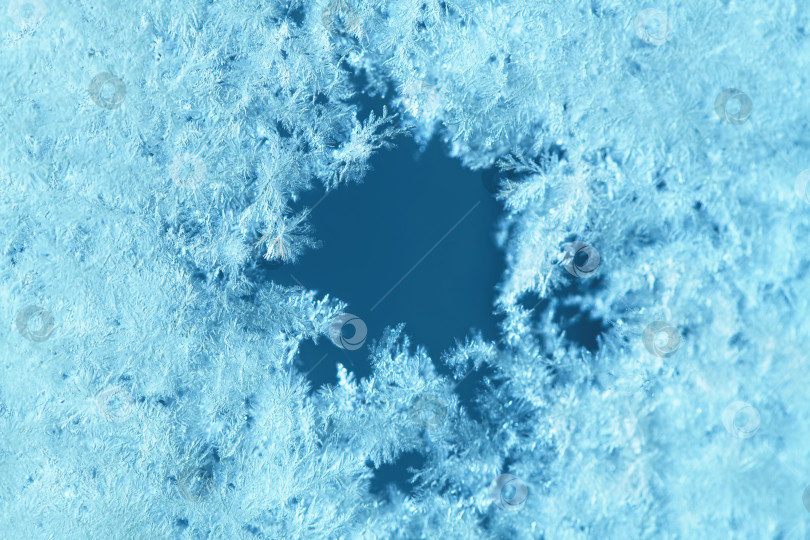 Скачать Кристаллы инея образуют замысловатые узоры вокруг темного центрального отверстия, создавая нежную естественную текстуру в прохладной голубой и бирюзовой палитре, символизируя объятия зимы и застывшие пейзажи. фотосток Ozero