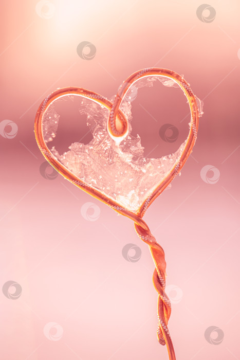 Скачать Нежный замороженный мыльный пузырь, образующий сердечко на медной проволоке, на фоне нежно-розового боке, морозные кристаллические текстуры, напоминающие о хрупкой любви, зимней романтике и мечтательной интимности фотосток Ozero