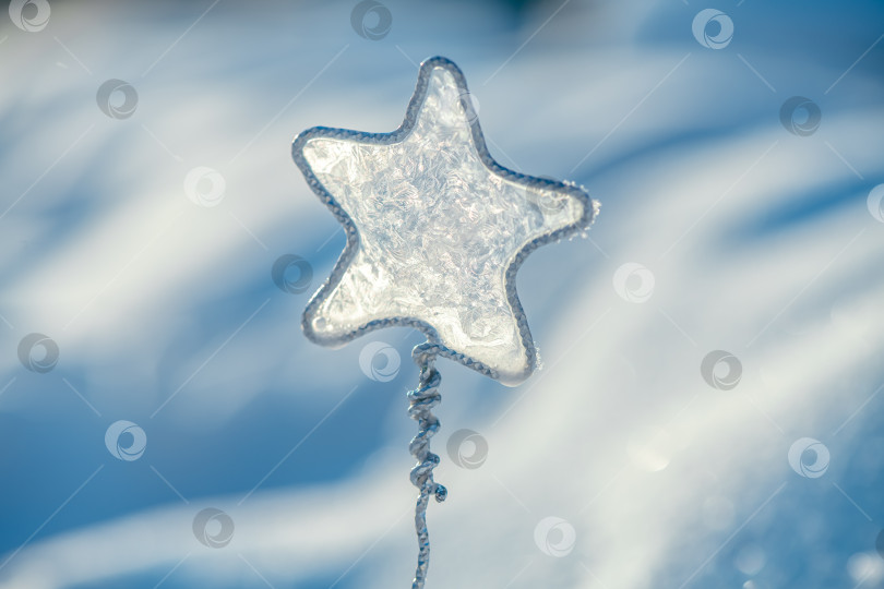 Скачать Сверкающий орнамент в виде ледяной звезды, стоящий вертикально на фоне морозного зимнего пейзажа, отражает солнечный свет на фоне мягкого бело-голубого боке, напоминая о волшебстве праздника и красоте холодного времени года. фотосток Ozero