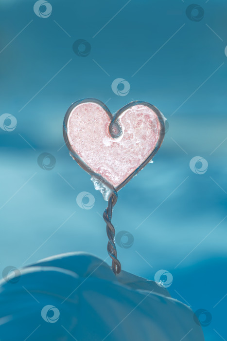 Скачать Скульптура розового замороженного сердца покоится на снежном сугробе, сверкая ледяной текстурой на холодном голубом зимнем фоне, навевая романтику, нежную красоту и сезонные эмоции оттепели фотосток Ozero