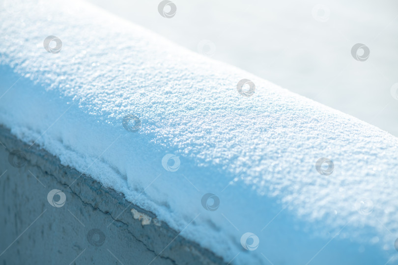 Скачать Свежий снег покрывает бетонные перила, сверкая в ярком зимнем солнечном свете и создавая четкие текстурные узоры на холодной, безмятежной поверхности улицы фотосток Ozero