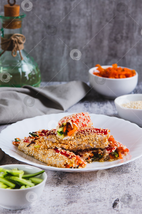 Скачать Огурцы и корейская морковь, завернутые в крабовое мясо и обжаренные с кунжутом, на тарелке в вертикальном положении фотосток Ozero