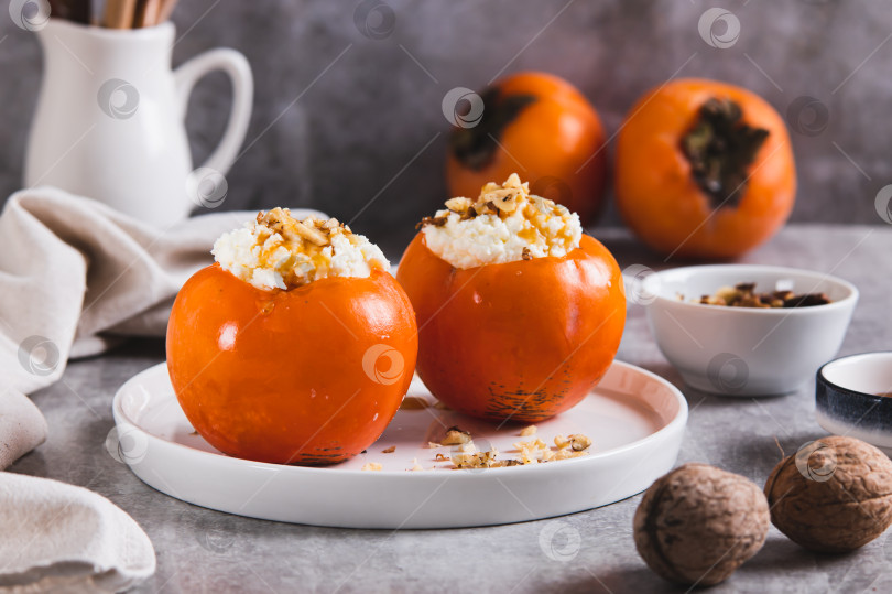 Скачать Спелая хурма с начинкой из творога, меда и орехов на тарелке на столе фотосток Ozero