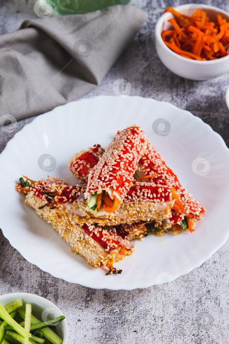 Скачать Запеченные крабовые рулетики с огурцом и морковью в кунжуте на тарелке в вертикальном положении фотосток Ozero