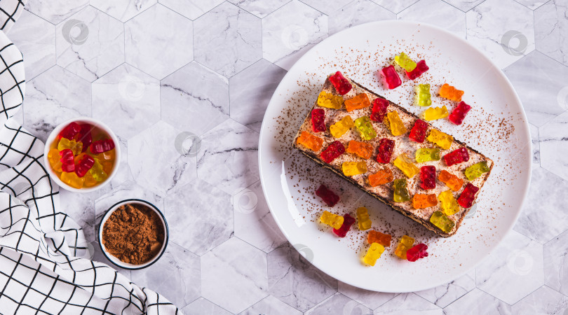 Скачать Сладкий тирамису с мармеладными мишками на тарелке на столешнице посмотреть веб-баннер фотосток Ozero