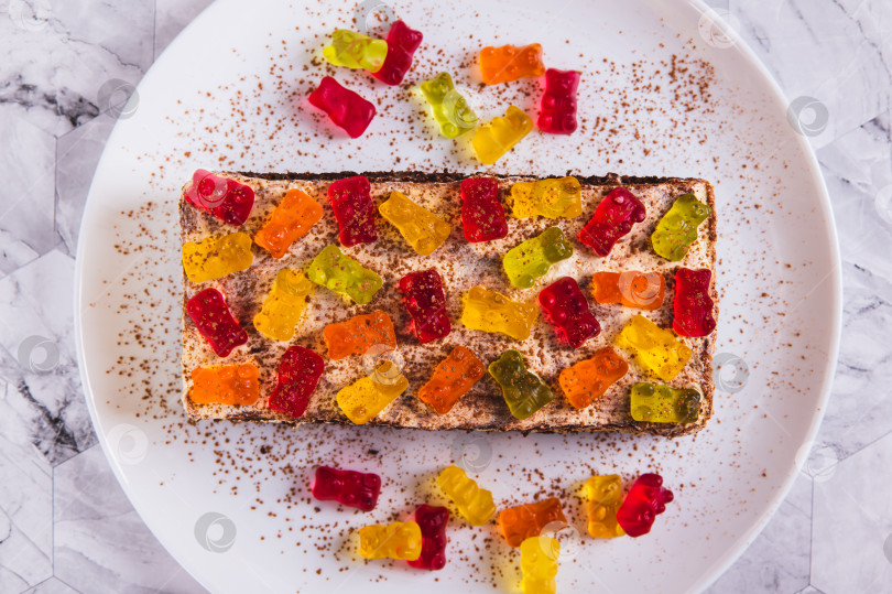 Скачать Крупный план шоколадного торта, украшенного мармеладными мишками, на тарелке на столе, вид сверху фотосток Ozero