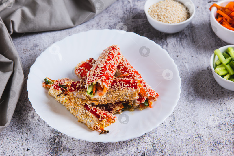 Скачать Запеченные крабовые рулетики с огурцом и морковью в кунжуте на тарелке на столе фотосток Ozero