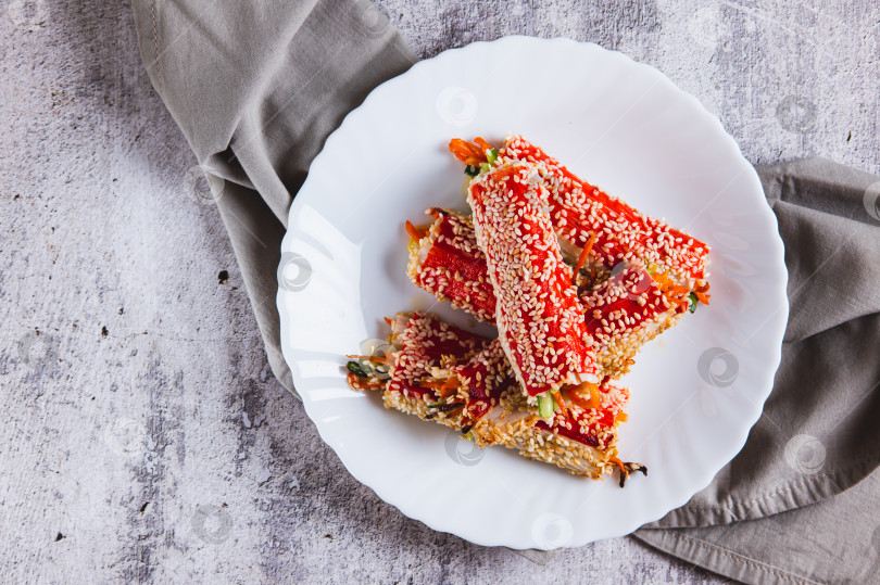 Скачать Крупным планом огурцы и морковь, завернутые в крабовое мясо и обжаренные с кунжутом на тарелке, вид сверху фотосток Ozero