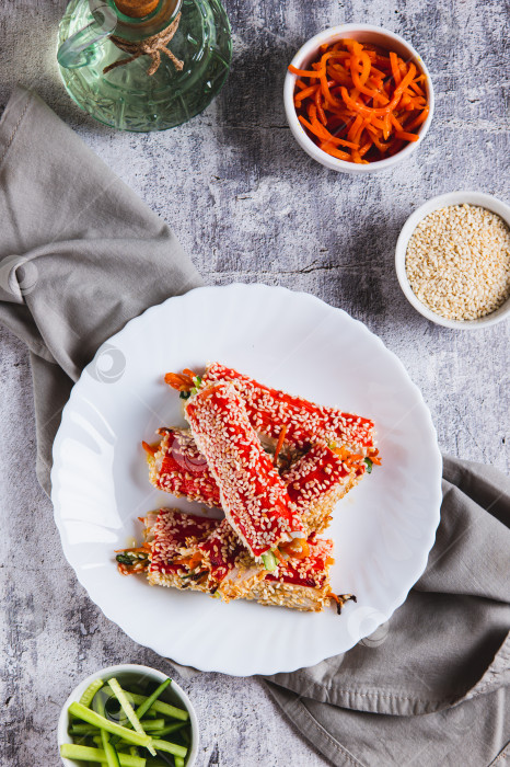 Скачать Запеченные крабовые рулетики с огурцом и морковью в кунжуте на тарелке в вертикальном положении фотосток Ozero