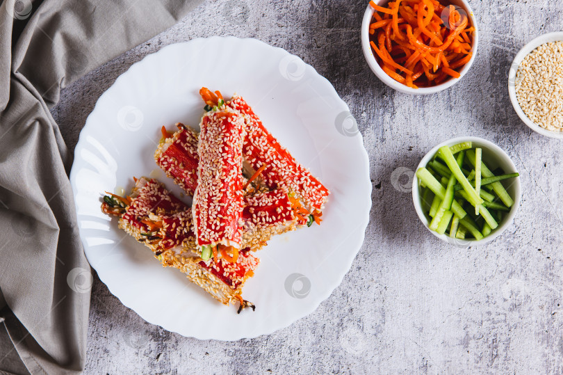 Скачать Огурцы и корейская морковь, завернутые в крабовое мясо и обжаренные с кунжутом на тарелке, вид сверху фотосток Ozero