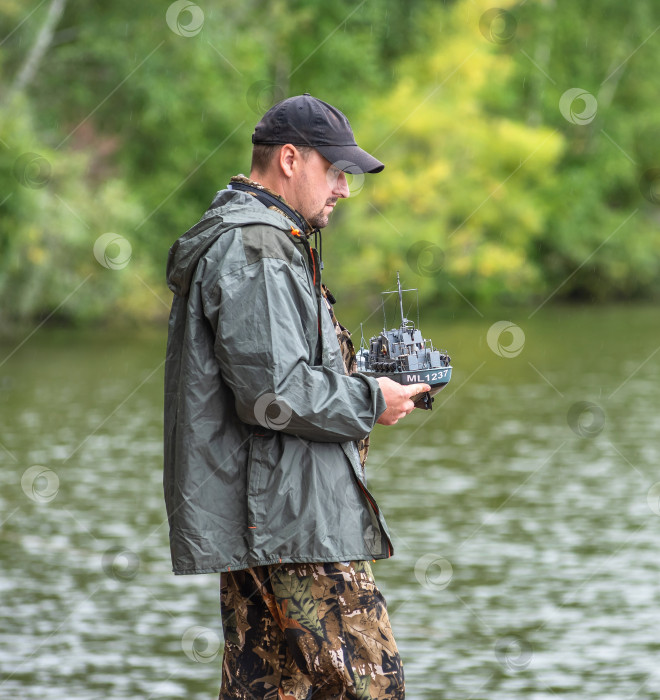 Скачать Россия,город Железногорск Красноярский Край, 26 августа 2023 год.Человек стоит у воды и держит в руках модель корабля. фотосток Ozero