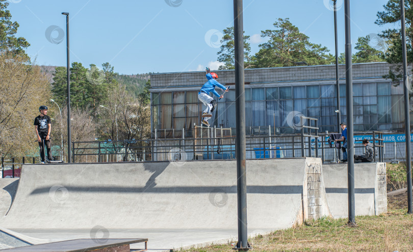 Скачать Россия, Красноярск 02 мая 2025г. Подросток на трюковом самокате в скейт-парке выполняет трюк во время прыжка. фотосток Ozero