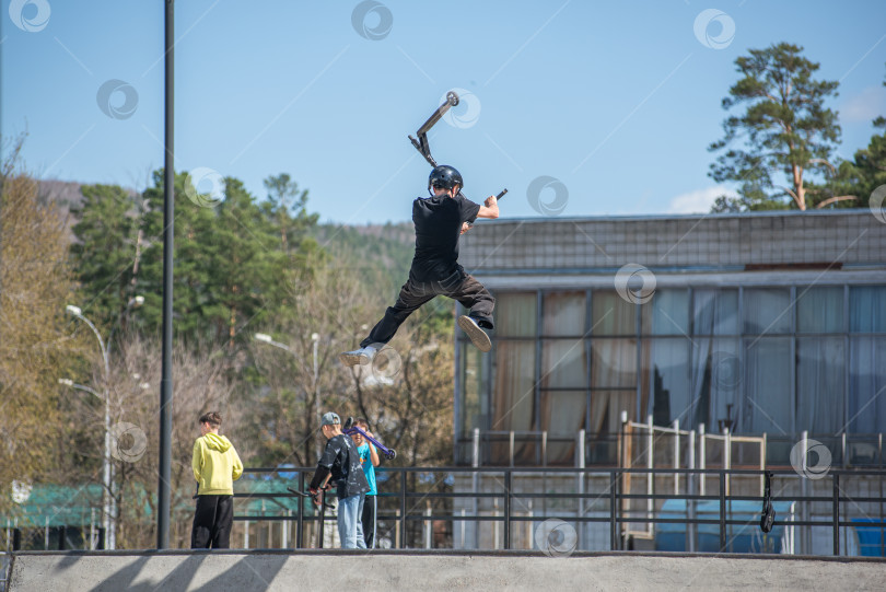 Скачать Россия, Красноярск 02 мая 2025г. Подросток на трюковом самокате в скейт-парке выполняет трюк во время прыжка. фотосток Ozero