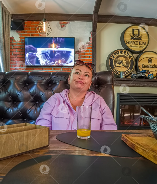 Скачать Россия,город Железногорск Красноярский Край, 26 августа 2023 год.женщина в розовой кофте сидит за столом в кафе. На столе стоит стакан с апельсиновым соком. фотосток Ozero