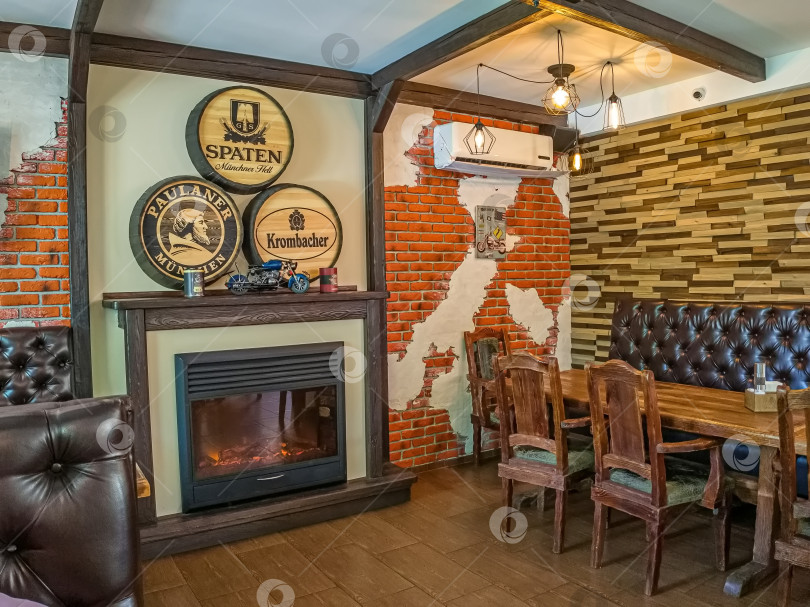 Скачать Россия,город Железногорск Красноярский Край, 26 августа 2023 год.Интерьер бара с камином, деревянными столами и стульями. Стены кирпичные и с декоративной отделкой. фотосток Ozero