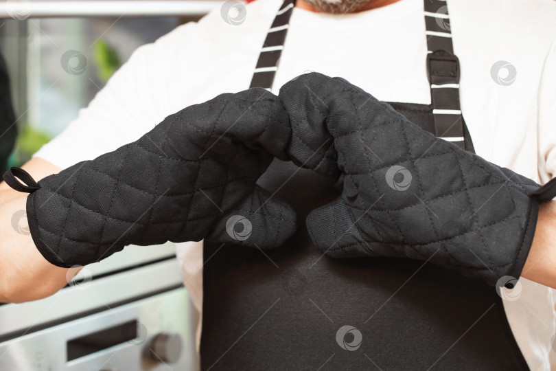 Скачать мужчина в черном поварском фартуке на кухне, на руках варежки фотосток Ozero