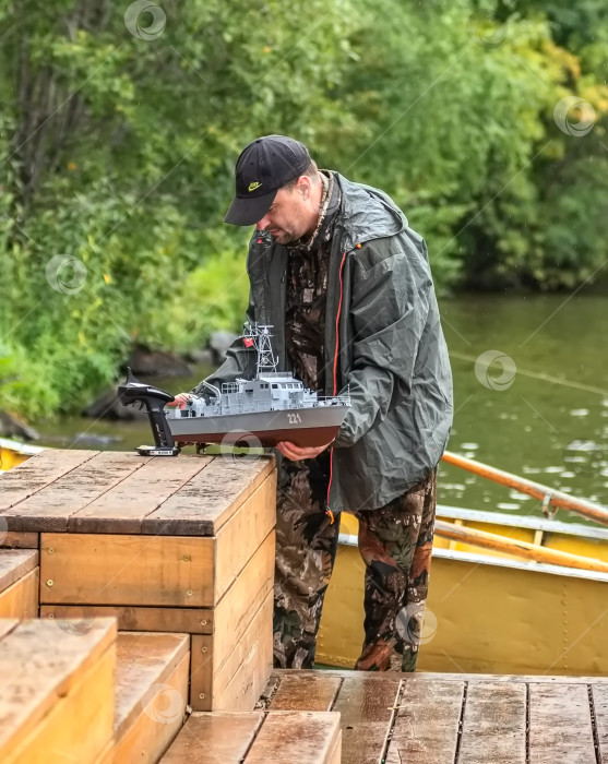 Скачать Россия,город Железногорск Красноярский Край, 26 августа 2023 год.Мужчина  держит в руках модель корабля, на причале у воды фотосток Ozero