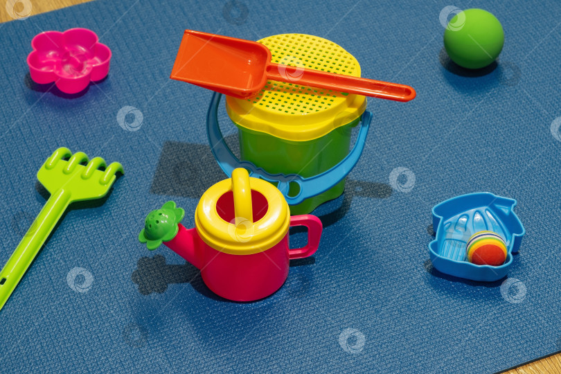 Скачать Красочные пластиковые игрушки для детей, разложенные на синем игровом коврике в помещении солнечным днем фотосток Ozero