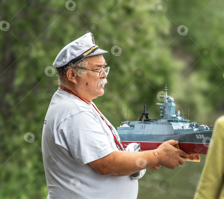 Скачать Россия,город Железногорск Красноярский Край, 26 августа 2023 год. Мужчина в капитанской кепке держит в руках модель военного корабля. фотосток Ozero