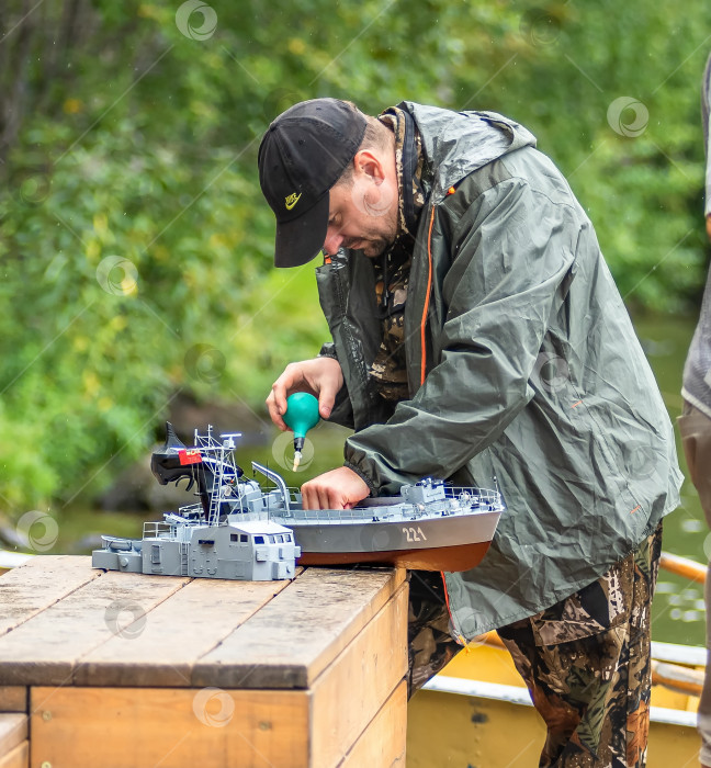 Скачать Россия,город Железногорск Красноярский Край, 26 августа 2023 год. Человек в кепке работает с моделью корабля на деревянной поверхности. фотосток Ozero