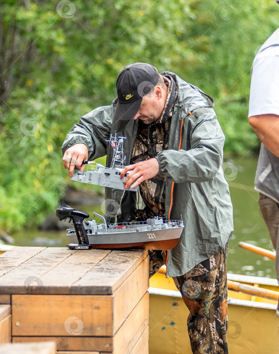 Скачать Россия,город Железногорск Красноярский Край, 26 августа 2023 год. Человек в кепке работает с моделью корабля на деревянной поверхности. фотосток Ozero