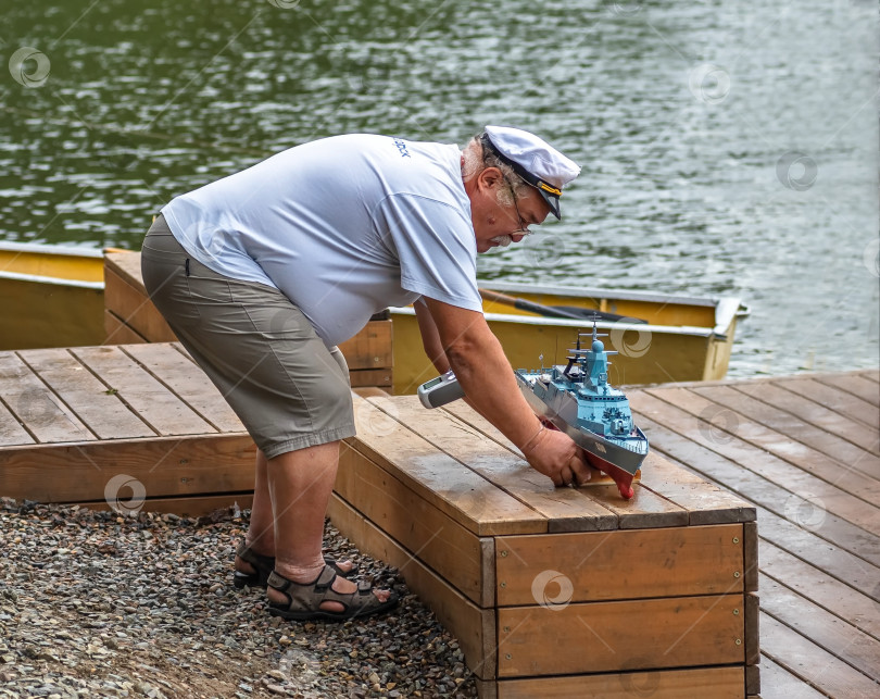 Скачать Россия,город Железногорск Красноярский Край, 26 августа 2023 год. Мужчина в капитанской кепке держит в руках модель военного корабля. фотосток Ozero