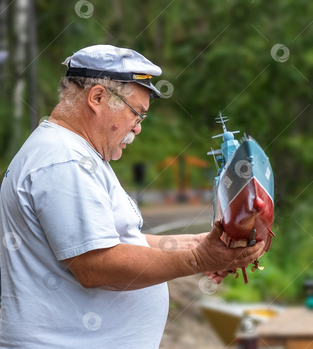 Скачать Россия,город Железногорск Красноярский Край, 26 августа 2023 год. Мужчина в капитанской кепке держит в руках модель военного корабля. фотосток Ozero