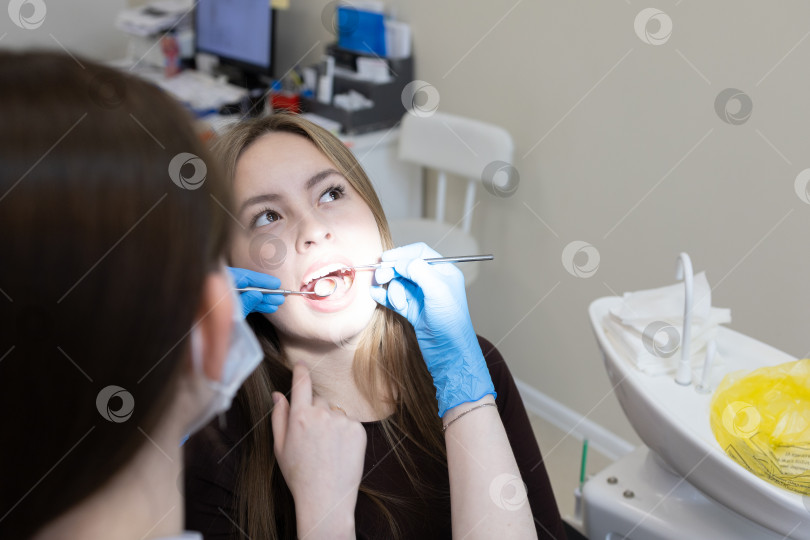 Скачать Симпатичная молодая женщина-стоматолог проводит обследование и лечение молодой пациентки в стоматологической клинике. фотосток Ozero