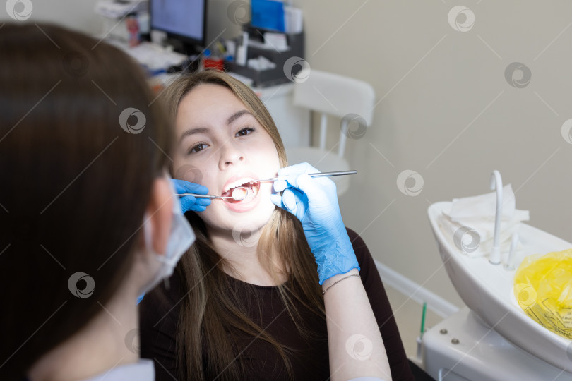 Скачать Симпатичная молодая женщина-стоматолог проводит обследование и лечение молодой пациентки в стоматологической клинике. фотосток Ozero