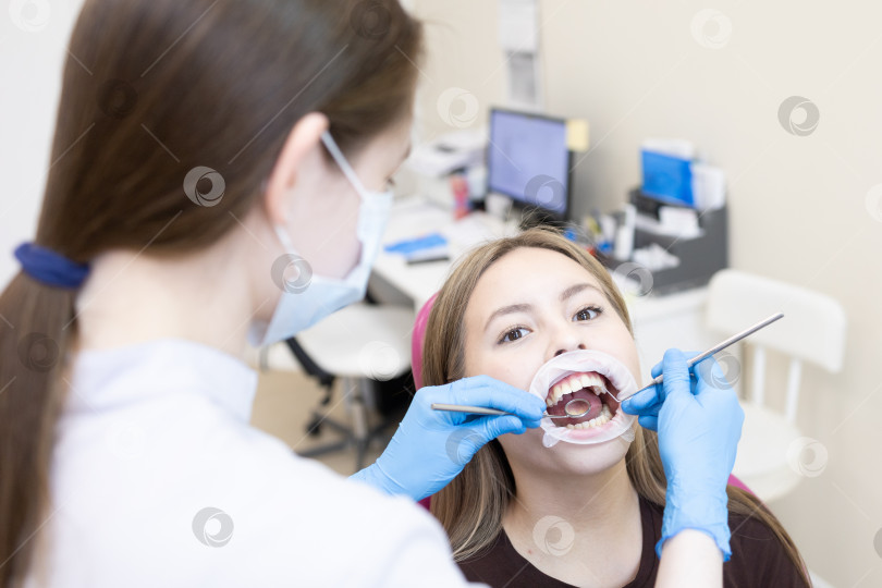 Скачать стоматолог устанавливает пациенту ретрактор. В современной стоматологической клинике стоматолог лечит зубы молодой женщины с помощью ротового ретрактора. фотосток Ozero