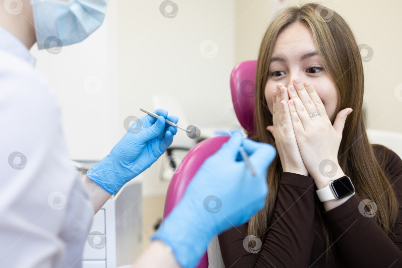 Скачать Пациентка боится стоматолога и закрывает рот руками. женщина, сидящая в стоматологическом кресле фотосток Ozero