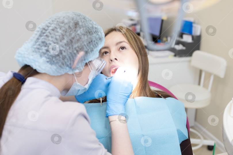 Скачать Симпатичная молодая женщина-стоматолог проводит обследование и лечение молодой пациентки в стоматологической клинике. фотосток Ozero