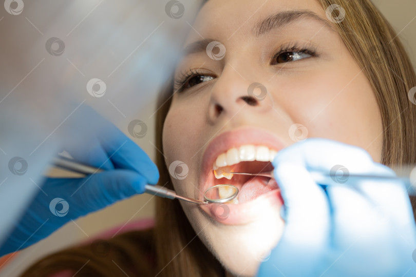 Скачать Симпатичная молодая женщина-стоматолог проводит обследование и лечение молодой пациентки в стоматологической клинике. фотосток Ozero