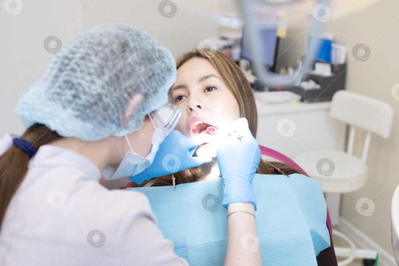 Скачать Симпатичная молодая женщина-стоматолог проводит обследование и лечение молодой пациентки в стоматологической клинике. фотосток Ozero