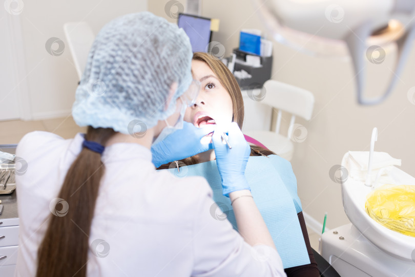Скачать Симпатичная молодая женщина-стоматолог проводит обследование и лечение молодой пациентки в стоматологической клинике. фотосток Ozero