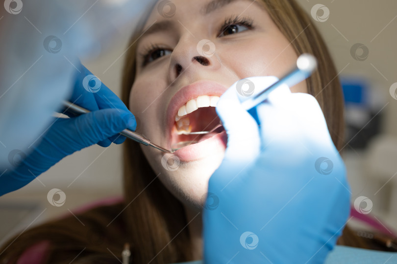 Скачать Симпатичная молодая женщина-стоматолог проводит обследование и лечение молодой пациентки в стоматологической клинике. фотосток Ozero