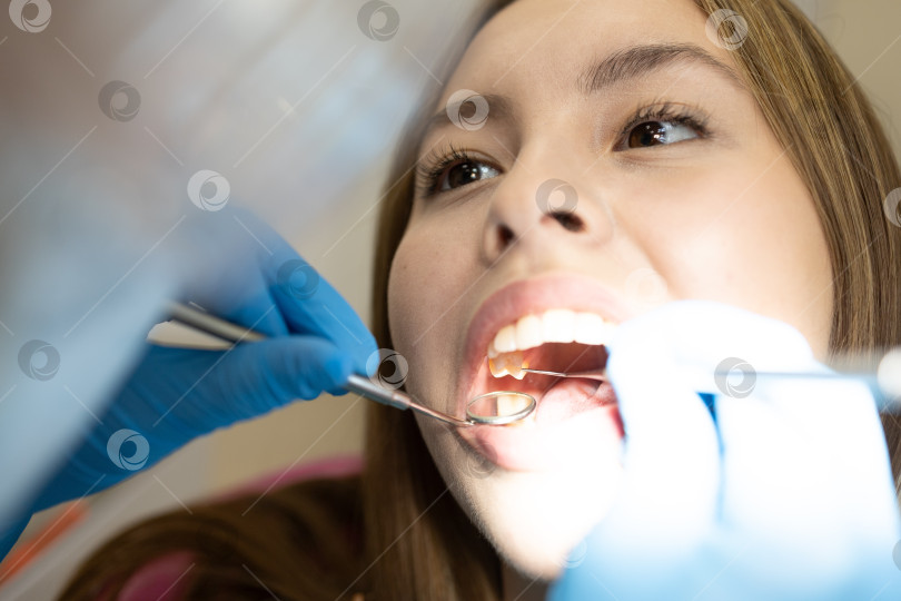Скачать Симпатичная молодая женщина-стоматолог проводит обследование и лечение молодой пациентки в стоматологической клинике. фотосток Ozero