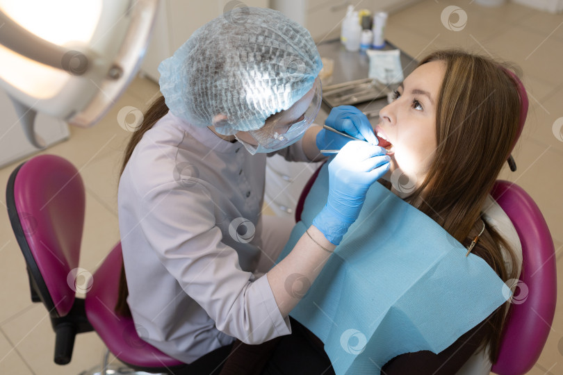 Скачать Симпатичная молодая женщина-стоматолог проводит обследование и лечение молодой пациентки в стоматологической клинике. фотосток Ozero