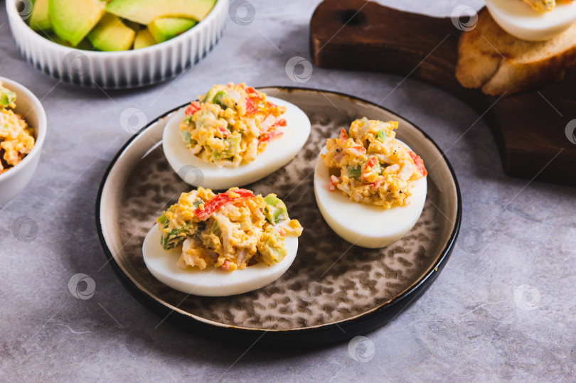 Скачать Пикантные яйца, фаршированные желтком, авокадо и помидорами, на тарелке на столе фотосток Ozero