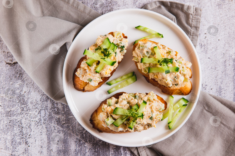 Скачать Бутерброды с салатом из печени трески, яйцом и огурцом крупным планом на тарелке на столе, вид сверху фотосток Ozero