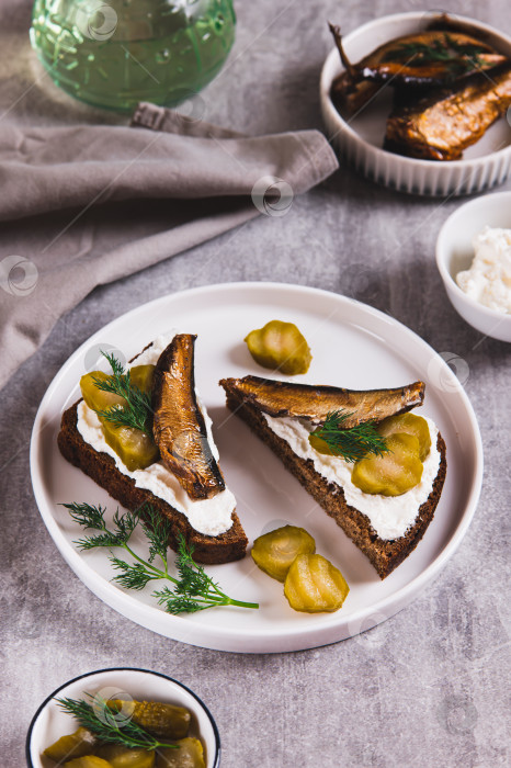 Скачать Тосты из ржаного хлеба со сливочным сыром, шпротами и солеными огурцами на тарелке на столе, вид сверху фотосток Ozero