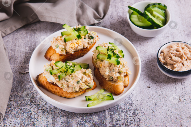 Скачать Салат из печени трески, яиц и огурцов с тостами на тарелке на столе фотосток Ozero